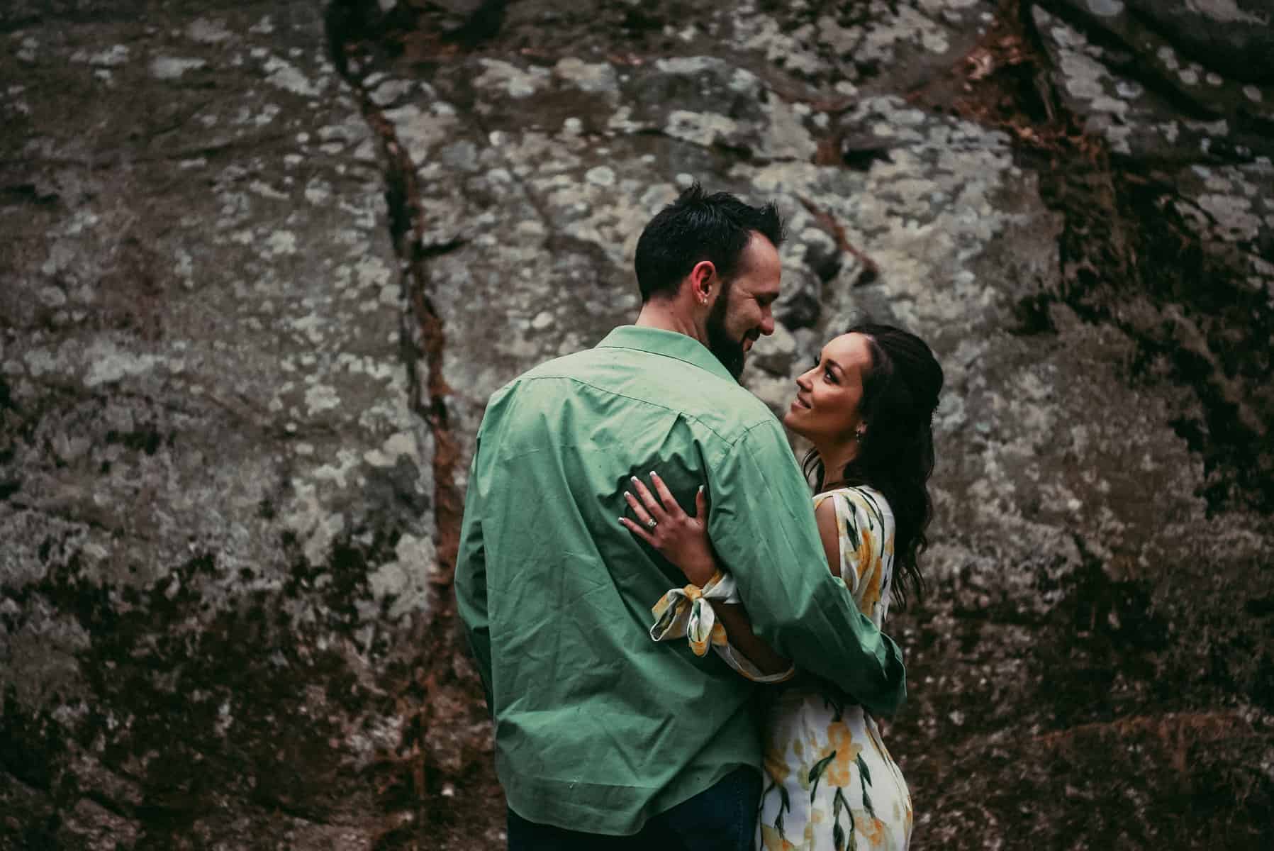 A man and woman gaze lovingly at each other with woods in the background.