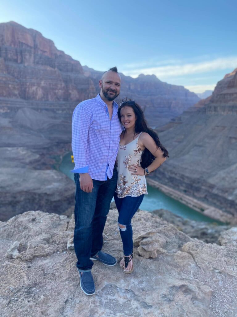 a couple stands in front of the Colorado River at the Grand Canyon