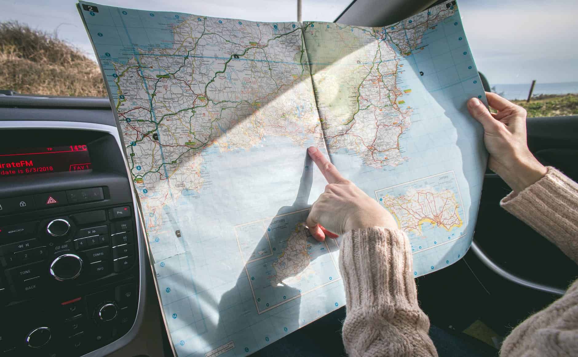 person wearing beige sweater holding map inside vehicle on road trip