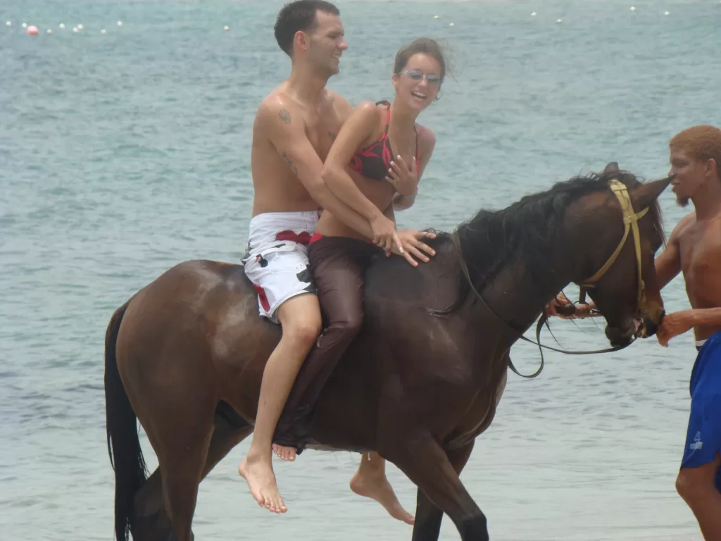 a laughing couple on a horse on the beach