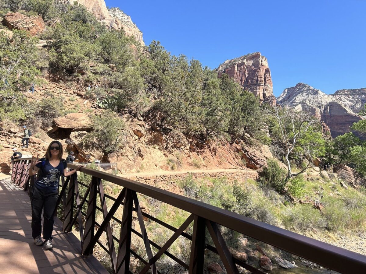 A woman standing on a bridge in Zion National Park with lots of trees in the background.