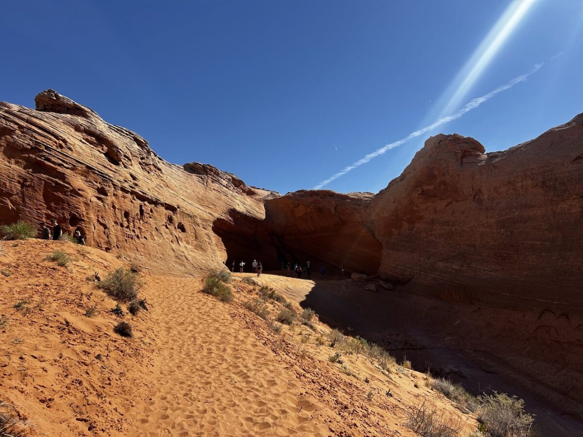 Red sand and rocks leading to the secret cave in Page, Arizona, with blue sky above.