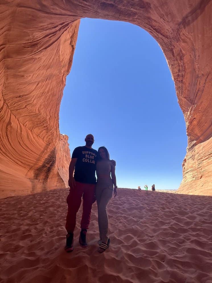 A man and woman inside the hidden cave in Page, Arizona, with blue sky seen behind them.